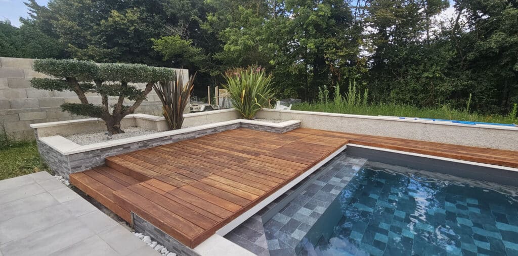 Piscine moderne et terrasse bois : l'aménagement extérieur Piscine rectangulaire moderne avec revêtement mosaïque bleue, entourée d'une terrasse en bois exotique, de jardinières en pierre et d'un olivier taillé.